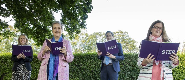 Four people spelling out 'Take the First Step' with books